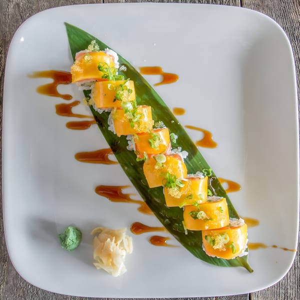Mango sushi rolls on a banana leaf, garnished with roe and scallions, with wasabi and ginger.