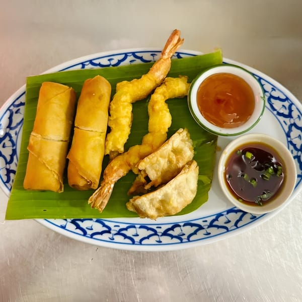 Crispy spring rolls, tempura shrimp, and dumplings with two dipping sauces on a banana leaf.