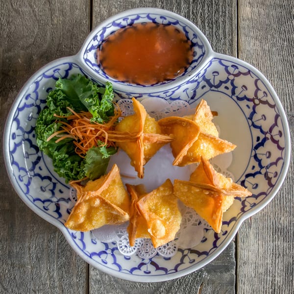 Crab rangoons with sweet chili sauce, kale, and shredded carrots on a decorative plate.