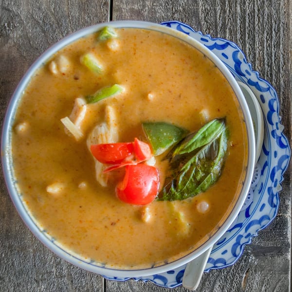 Close-up of Thai red curry with chicken, tomatoes, and basil in a decorative bowl.