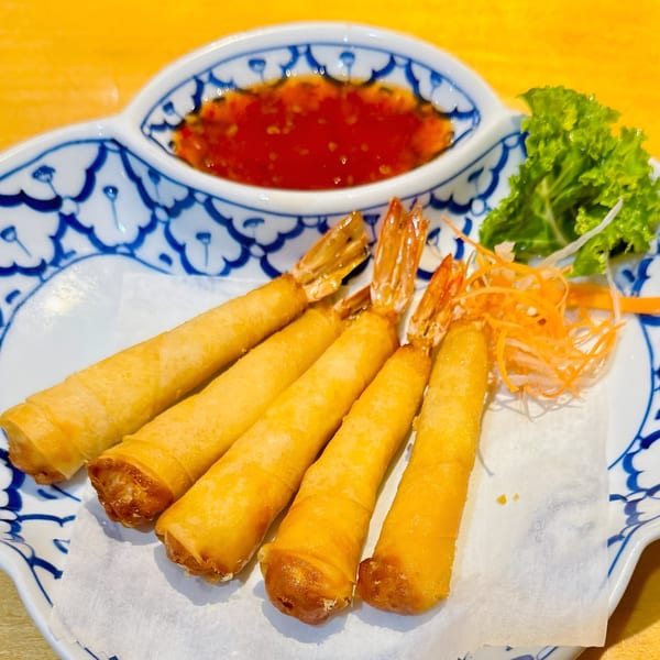 Five crispy shrimp spring rolls with tails, served with sweet chili sauce and lettuce on a blue and white plate.